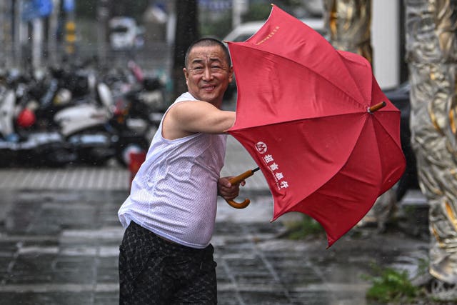 A man holding a red umbrella struggles against the wind