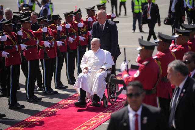 Pope Francis, in his wheelchair, is welcomed by members of the honour guard at Dili Presidente Nicolau Lobato International Airport in Dili, East Timor 