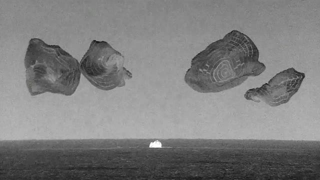 Black and white thermal image showing capsule landing at sea, with four parachutes above it