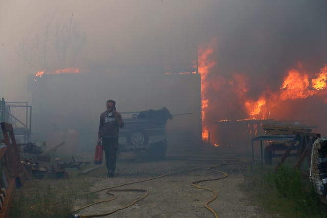 A man carries a fire extinguisher amid a blaze and thick smoke in Portugal