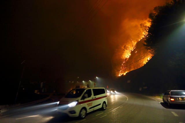 Vehicles drive past a fire burning by the road near a town in northern Portugal