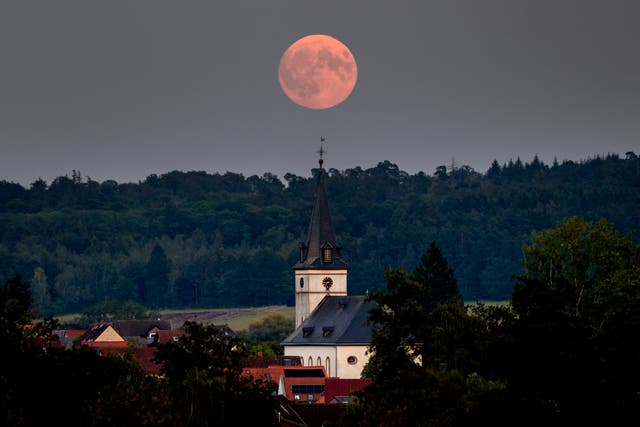 The full Harvest moon rises behind the church in Wehrheim near Frankfurt