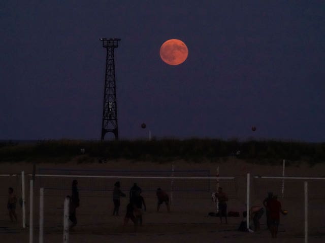 The pumpkin-coloured Harvest moon rises over the beach as people play volleyball on the shore of Lake Michigan