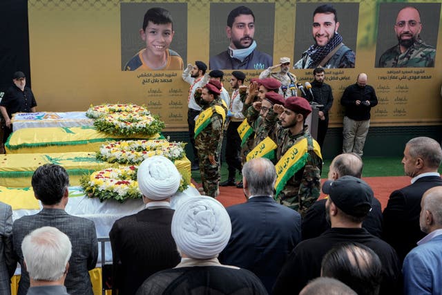 Hezbollah fighters salute as they stand next to the coffins of four victims who were killed Tuesday after their handheld pagers exploded, during their funeral procession in the southern suburb of Beirut 