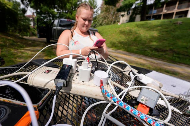 A woman looks at her phone as a neighbour with power dropped an extension cord for residents who have no power in Asheville 