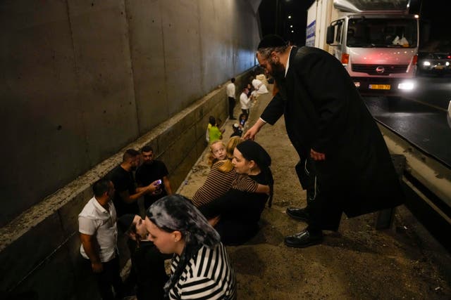 People take cover on the side of a road as a siren sounds a warning of incoming missiles fired from Iran in Shoresh, between Jerusalem and Tel Aviv in Israel on Tuesday