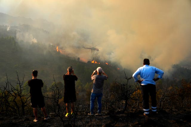 People watch and take photos of a helicopter dropping water on the flames 