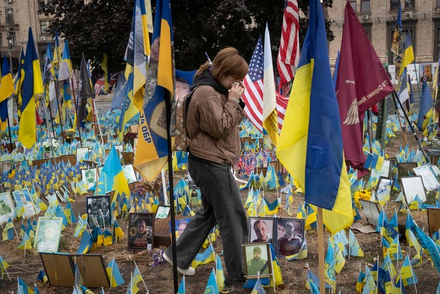 A persons wipes their nose as they walk past Ukrainian flags and photos of people who have died at an improvised war memorial in Independence Square in Kyiv 