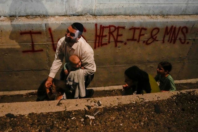 People take cover on the side of the road as a siren sounds a warning of incoming missiles fired from Iran on a freeway in Shoresh