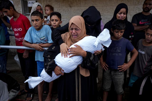 A woman cries while holding a child's body wrapped in a shroud 