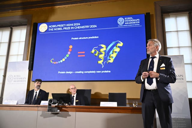 Johan Aqvist, right, of the Nobel Committee for Chemistry, uses a chart to explain the work of this year's prize winners, as fellow committee members look on