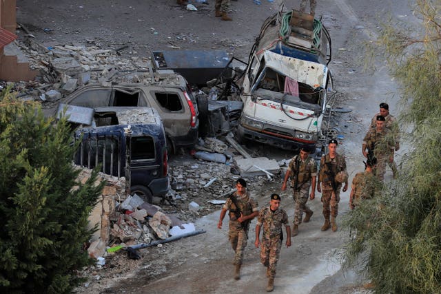 Lebanese army soldiers walk by destroyed cars