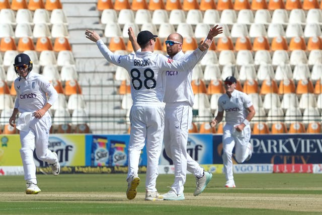 England’s Jack Leach celebrates with team-mate Harry Brook, both with arms raised, after taking the wicket of Pakistan’s Abdullah Shafique