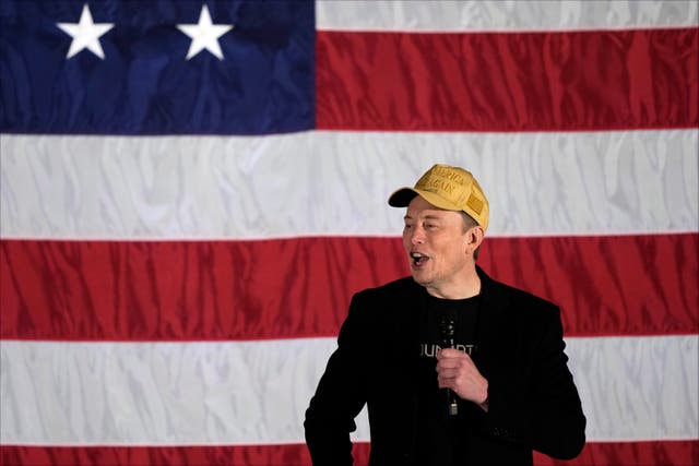 Elon Musk speaks in front of a giant Stars and Stripes flag