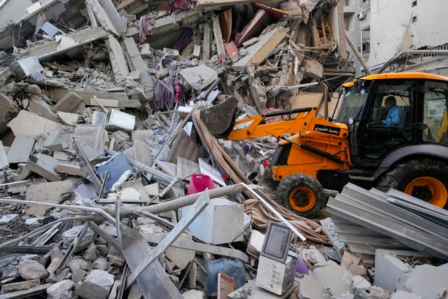 Rescue workers use a bulldozer to remove rubble of destroyed buildings at the site of an Israeli air strike