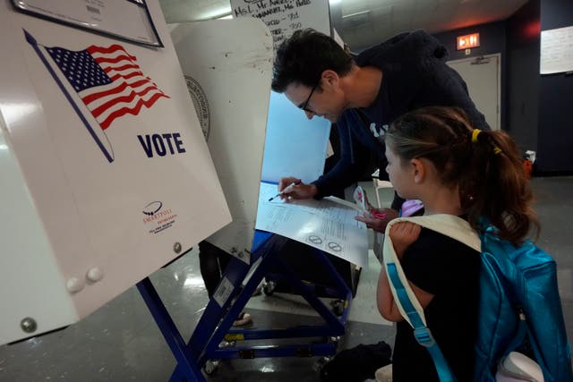 Benay Gould, seven, watches as her father Charles Herschel marks his ballot at PS M811, The Mickey Mantle School in New York 