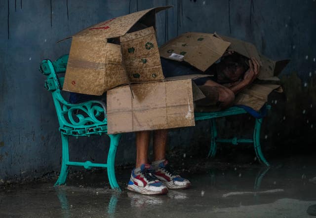 People at a bus stop shield themselves with cardboard from the wind and rain during the passage of Hurricane Rafael in Havana