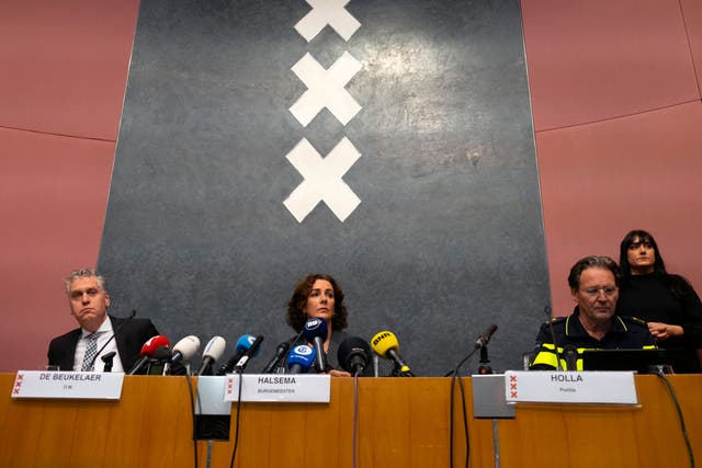 Woman and two men sitting behind a desk, speaking into microphones