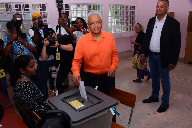 Pravind Jagnauth wearing orange shirt posts voting paper into ballot box