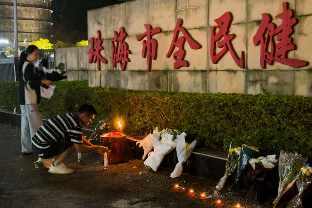 A man lights a candle near flowers placed outside the Zhuhai People’s Fitness Plaza