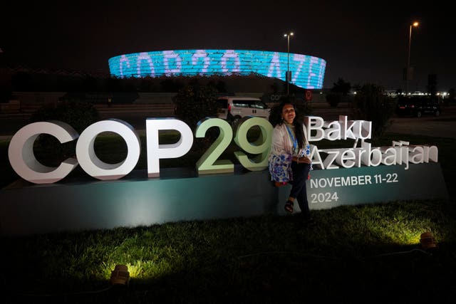 A woman poses in front of an illuminated Cop29 sign at night