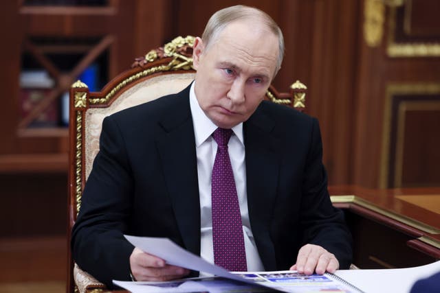 Russian President Vladimir Putin sits at a desk, holding pieces of paper in his right hand 