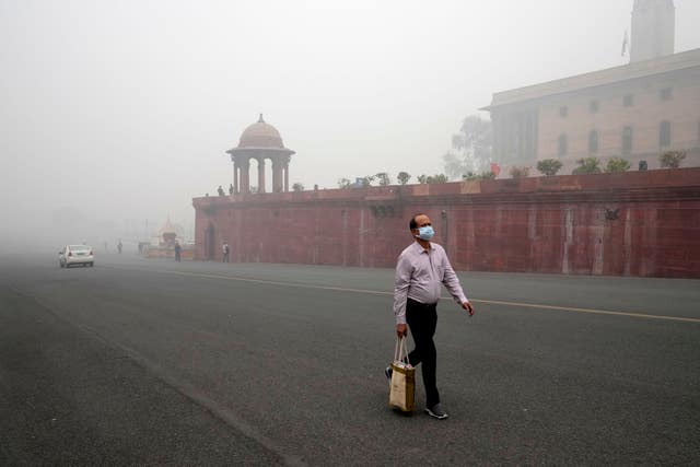 A office goer walks wearing a face mask amid a thick layer of smog in New Delhi