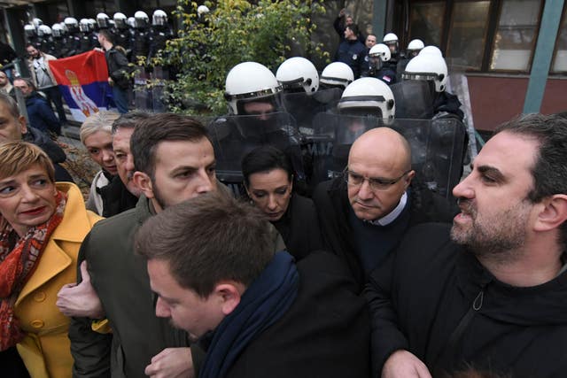 A line of protesters with white-helmeted riot police in the background