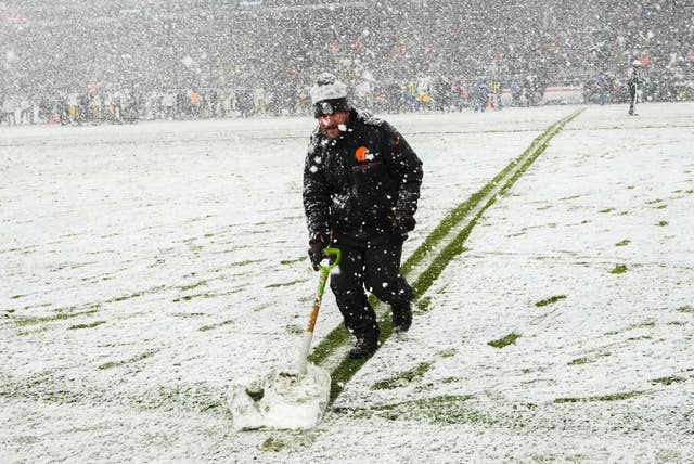 A groundskeeper shovels snow on the field in the second half