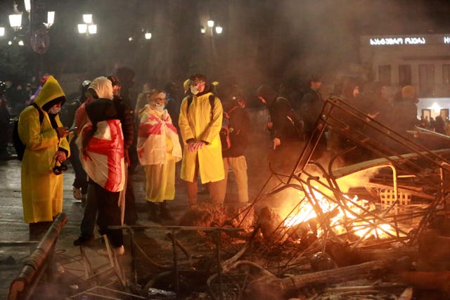 Demonstrators warm themselves next to a burning barricade 