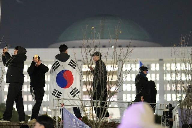 A man wearing a national flag stands on the wall of the National Assembly in Seoul, South Korea