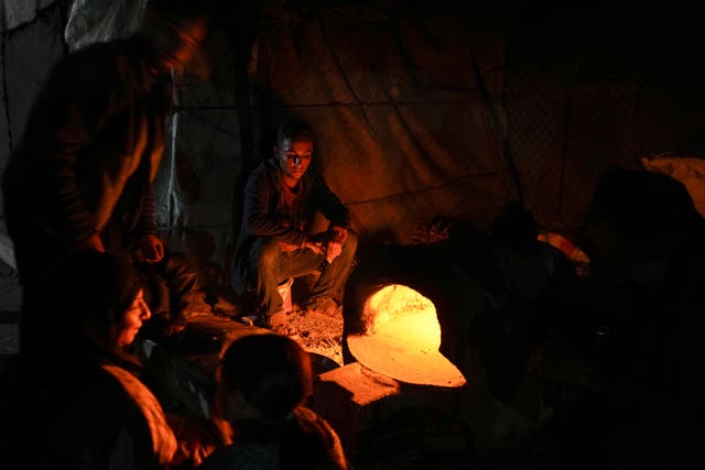 Displaced Palestinians sit next to an makeshift oven