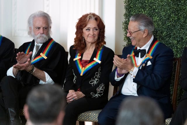 Grateful Dead band member Bobby Weir, left, and jazz trumpeter, pianist, and composer Arturo Sandoval, right, applaud blues rock singer-songwriter and guitarist Bonnie Raitt, centre