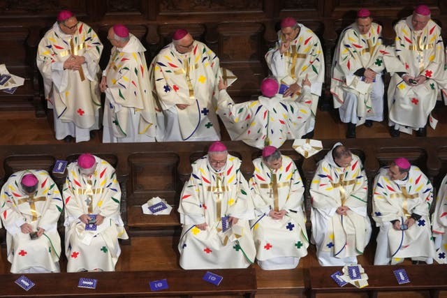 Clergy members in white robes sit on benches