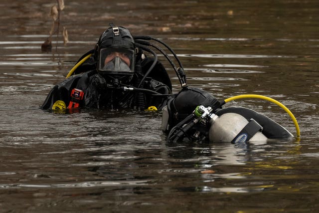 Two divers in full gear dip their heads into the brown-grey water of a Central Park pond