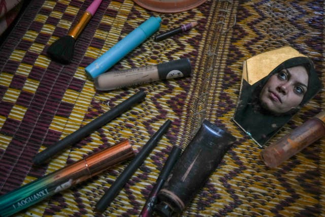 Alaa Hamami gazes into a fragment of a broken mirror as she poses for a portrait beside her deteriorating cosmetics in her tent at a camp for displaced Palestinians in Deir al-Balah, Gaza Strip