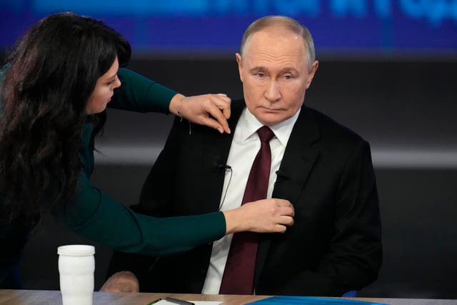 A woman adjusts Vladimir Putin's jacket as he prepares for his annual news conference