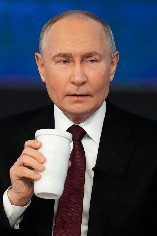 Vladimir Putin, holding a drink, listens to a question during his annual news conference