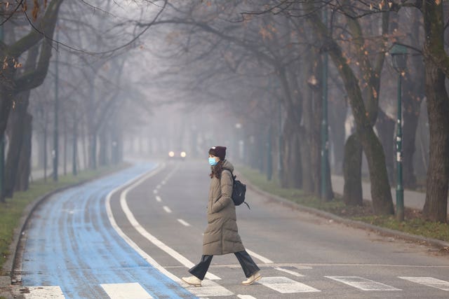 A woman wears a face mask shrouded by pollution haze as smog covers Sarajevo