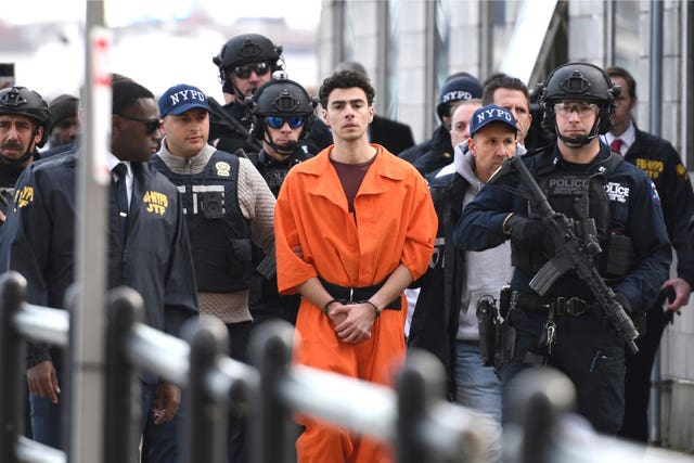 Luigi Mangione in cuffs and an orange prison suit is escorted to court by armed officers