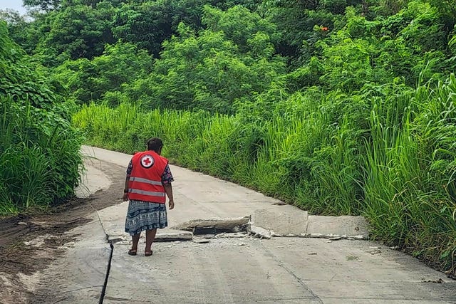 In this photo released by Vanuatu Red Cross Society, a volunteer inspects a damaged road in Efate, Vanuatu