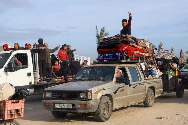 Man with arm raised on top of truck packed with belongings