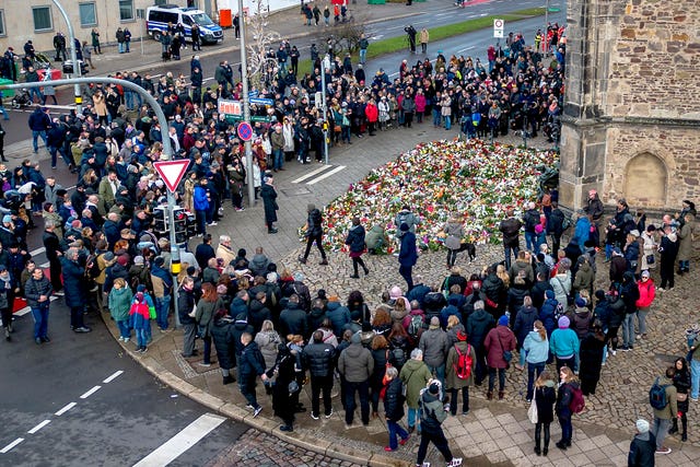 Crowd of people gathered around makeshift memorial of flowers and candles