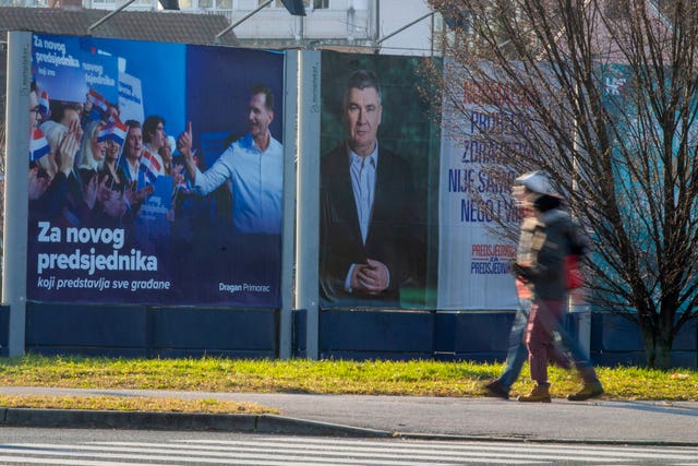 Pedestrians walk past campaign posters of presidential candidates Dragan Primorac and Zoran Milanovic 