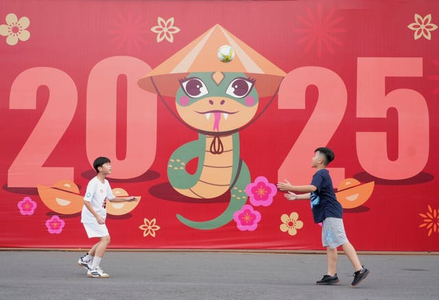 Two boys play football in front of a billboard welcoming the New Year 2025 in Ho Chi Minh city, Vietnam