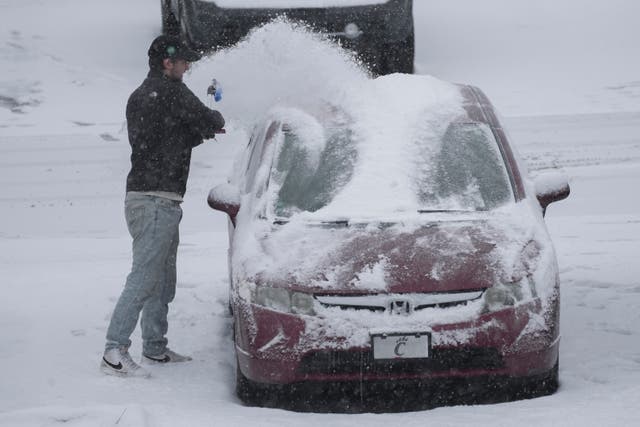 A person dusts snow off a car 