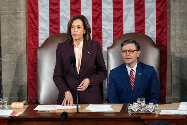 Kamala Harris and Mike Johnson sit in front of a huge American flag