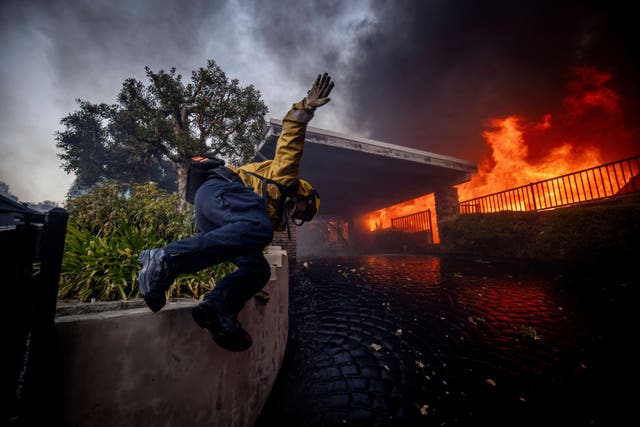 A firefighter jumps over a fence while fighting the Palisades Fire in the Pacific Palisades neighborhoo