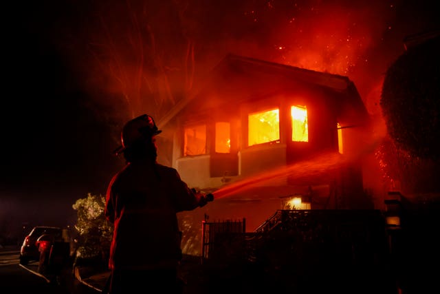 A firefighter works as the Palisades fires burn a house