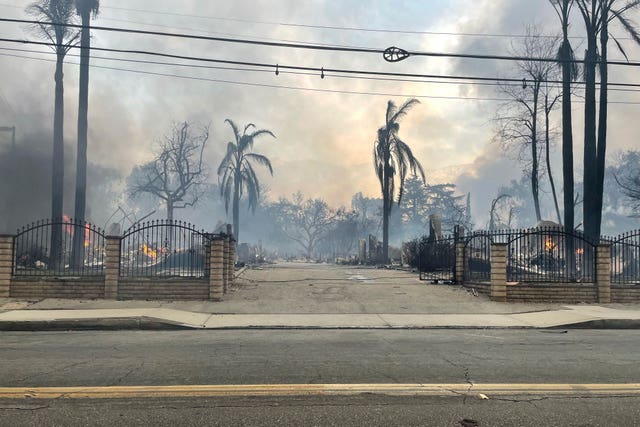 The entrance to what was once a beautiful ornate house. The only thing left standing is the wall and the gate. Behind that are burnt palm trees and a sky filled with smoke